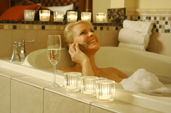 Женщина в ванной с шампанским и телефоном — стоковое фото
