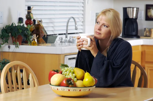 Созерцательная женщина на кухне с кружкой — стоковое фото