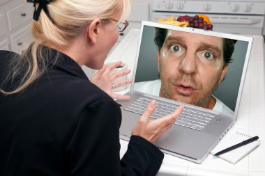 Shocked Woman In Kitchen Using Laptop with Strange Man on Screen clipart