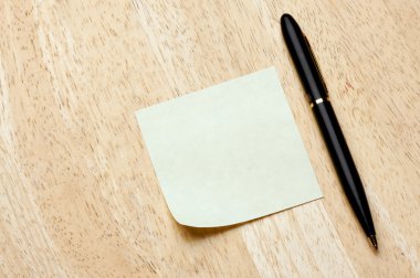 Pen and Post It Notes Pad Against a Wood Background clipart