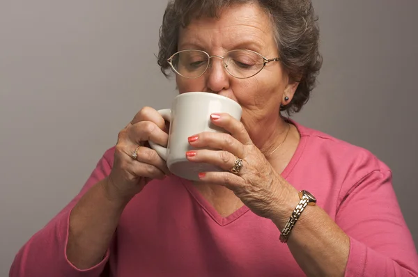 Mujer mayor en un fondo gris disfruta del café —  Fotos de Stock