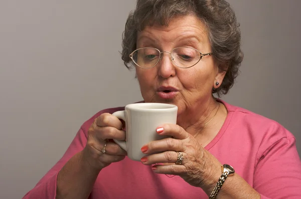 Mujer mayor en un fondo gris disfruta del café — Foto de Stock