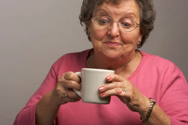 Äldre kvinna på en grå bakgrund har kaffe — Stockfoto