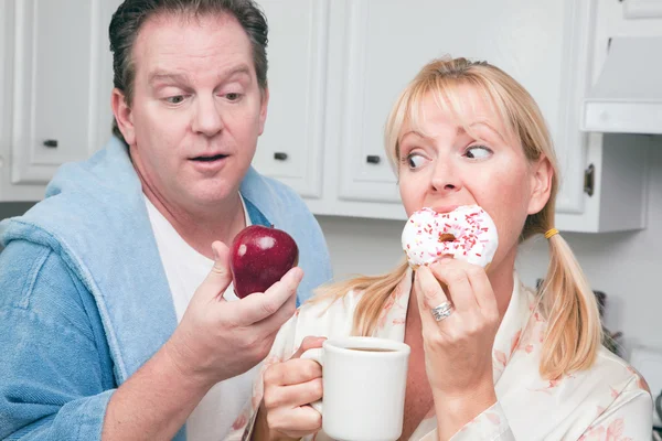 Dvojice v kuchyni jíst koblihy vs ovoce — Stock fotografie