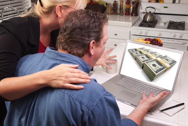 Пара на кухне с ноутбуком и стопки денег на экране — стоковое фото
