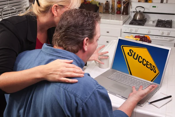 Пара на кухне с помощью ноутбука с желтым знаком успеха на экране — стоковое фото