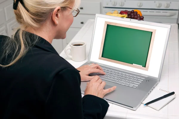 Жінка на кухні, використовуючи ноутбук з пустим дошці на екрані — стокове фото
