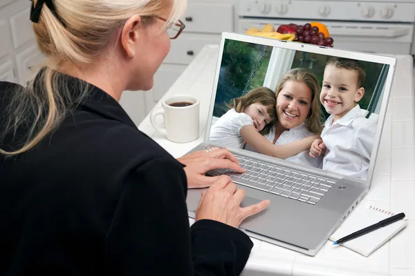 Kobieta w kuchni za pomocą laptopa z kobieta i dzieci na ekranie — Zdjęcie stockowe