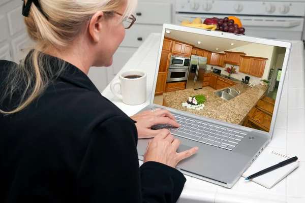 Femme dans la cuisine utilisant un ordinateur portable avec l'intérieur de la cuisine à l'écran — Photo