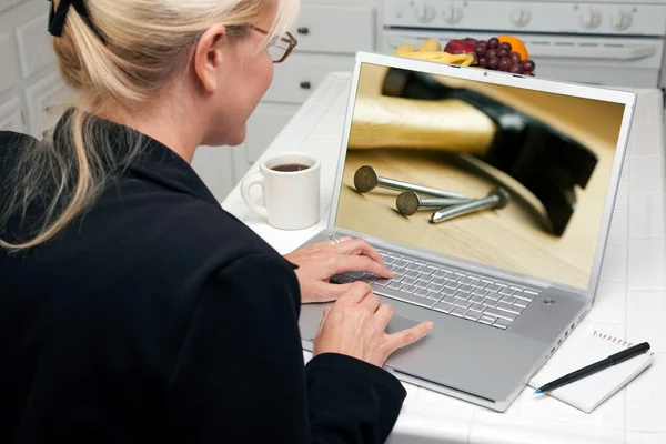 Kvinnan i köket använder bärbar dator med hammare och spik på skärmen — Stockfoto