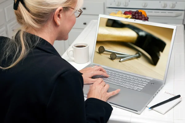 Mulher na cozinha usando computador portátil com martelo e unhas na tela — Fotografia de Stock