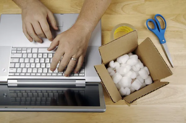 Man op laptop met verpakkende materialen — Stockfoto