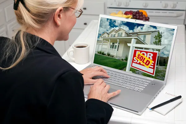 Mujer en la cocina usando el ordenador portátil para investigar bienes raíces — Foto de Stock