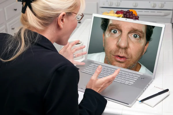 Шокована жінка на кухні за допомогою ноутбука з дивним чоловіком на екрані — стокове фото