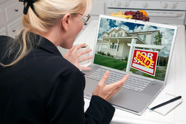 Збуджений жінка на кухні, використовуючи ноутбук продати або купити будинок — стокове фото