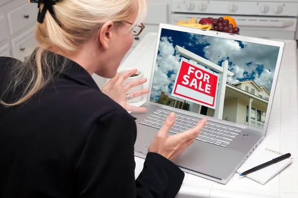 Захоплена жінка на кухні використовуючи ноутбук купити будинок — стокове фото