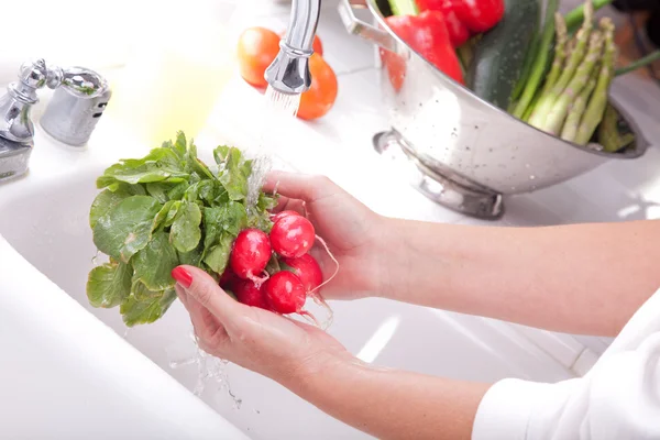 Женщина стирает редис в раковине на кухне — стоковое фото