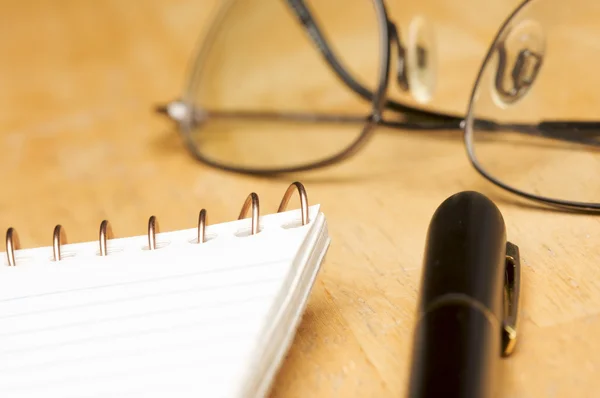 Ручка, блокнот и очки на фоне дерева — стоковое фото
