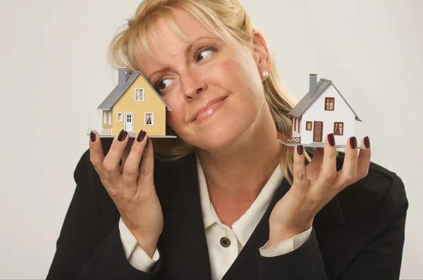 Mujer sonriente sosteniendo dos casas modelo — Foto de Stock
