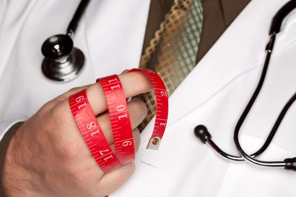 Médico con estetoscopio que sostiene cinta métrica roja — Foto de Stock