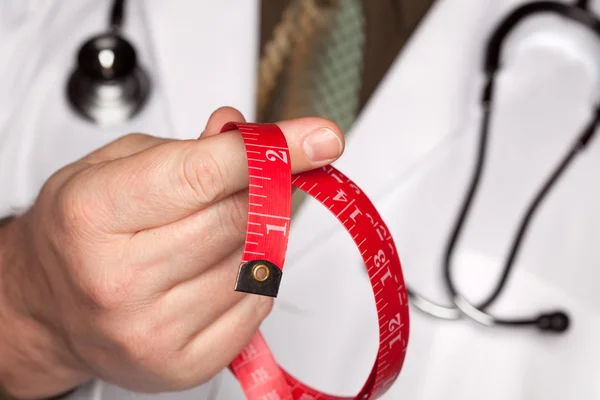 Doutor com estetoscópio segurando fita de medição vermelha — Fotografia de Stock