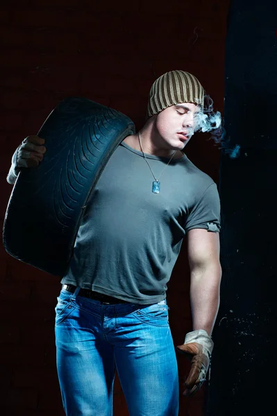 Young muscular man with tire smoking — Stock Photo, Image
