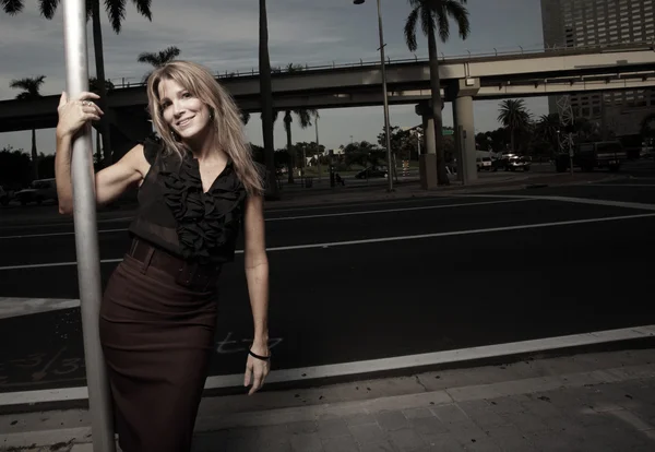 Frau posiert an einer Stange auf der Straße und lächelt — Stockfoto