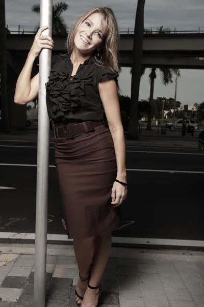 Mulher posando por um poste na rua e sorrindo — Fotografia de Stock