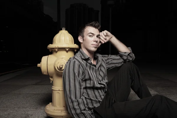 Man sitting by a fire hydrant at night — Stock Photo, Image