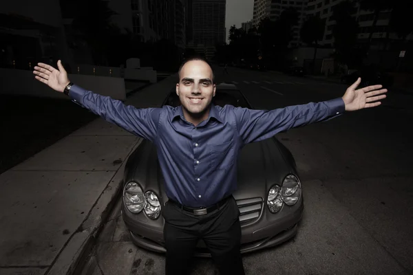 Businessman with arms extended and a luxury car in the background — Stock Photo, Image