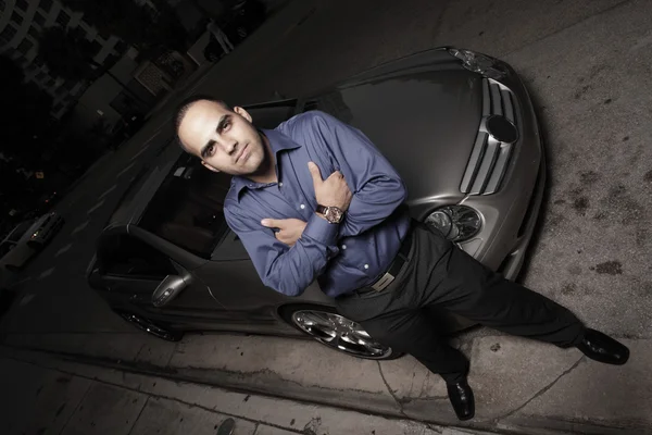Empresário posando por um carro esportivo de luxo e gesticulando com um polegar para cima — Fotografia de Stock