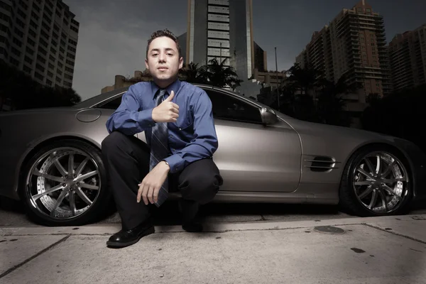 Empresário posando por um carro esportivo de luxo e gesticulando com um polegar para cima — Fotografia de Stock