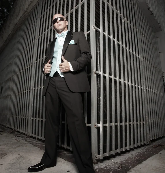 Man in a tuxedo posing by a metal enclosure — Zdjęcie stockowe