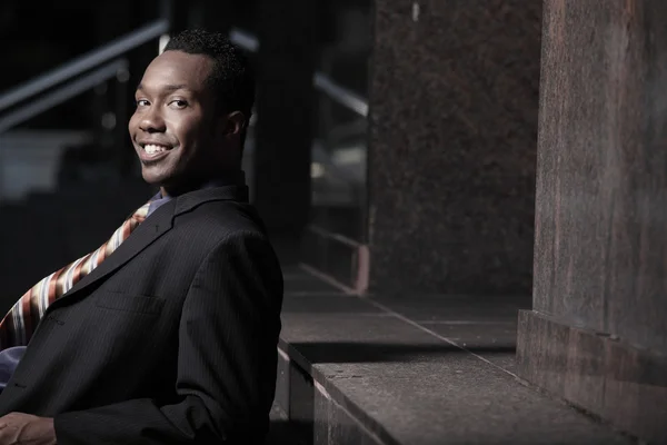 Junger afrikanisch-amerikanischer Geschäftsmann sitzt und lächelt — Stockfoto