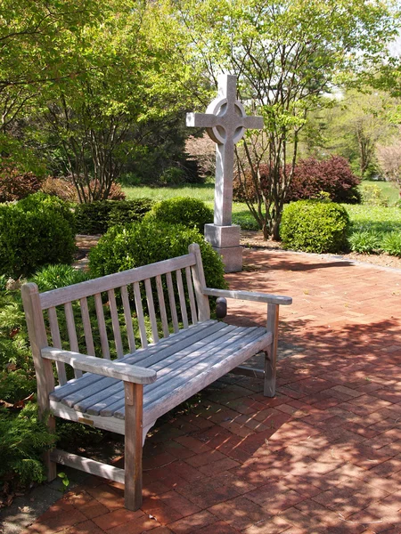 Empty wood bench by a cross and patio — Stock Photo, Image