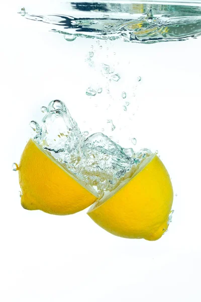 Eine in Scheiben geschnittene Zitrone fällt ins klare Wasser — Stockfoto