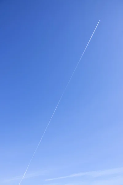 Airplane high up in blue sky with smoke