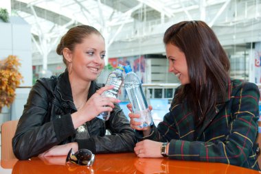 Two girls drink water in food court clipart