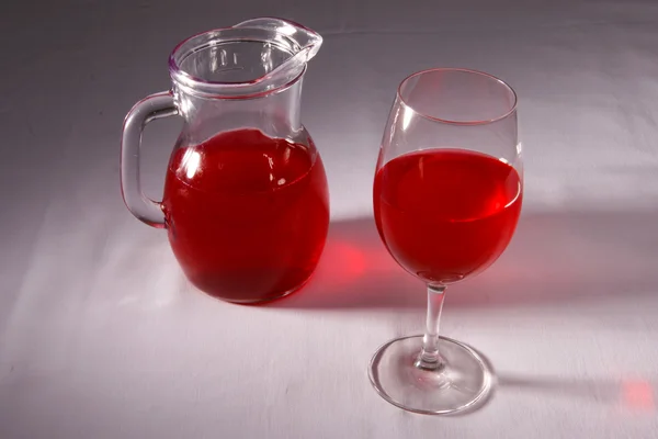 Bebida vermelha em um copo e um jarro — Fotografia de Stock