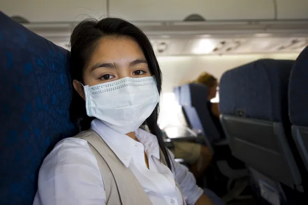 飛行機で防護マスクを持つ女性 ロイヤリティフリーのストック写真