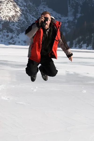 Main in red with photo jumping on winter mountai — Stock Photo, Image