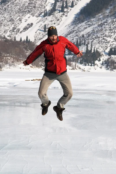 Main in red jumping on winter mountain lake — Stock Photo, Image