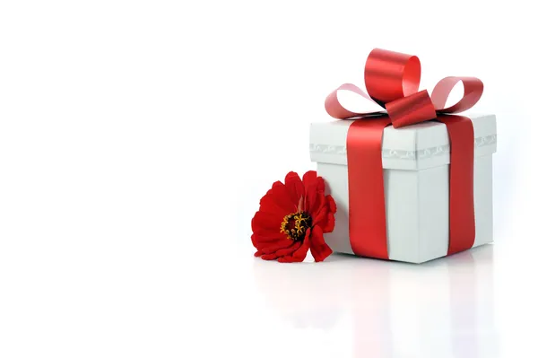 Подарок с красной лентой и цветком — стоковое фото