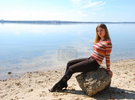 Fille assis à la pierre sur la plage de la rivière 